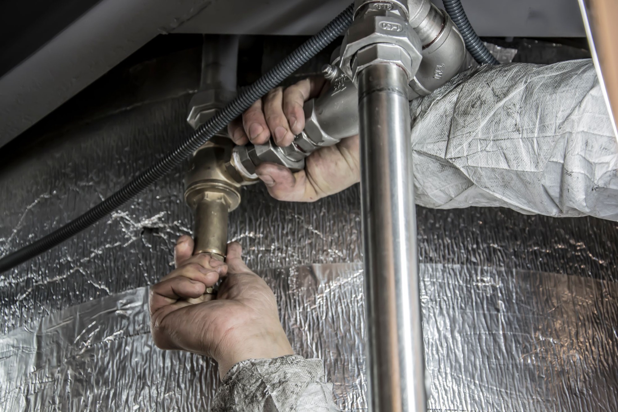 A heating engineer's hands tightening a brass valve onto insulated flow and return pipework
